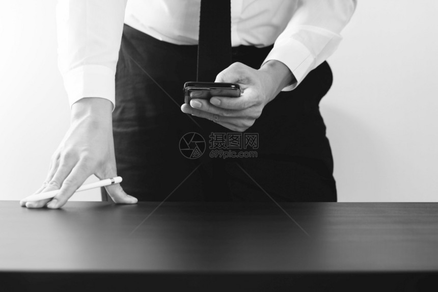 在现代办公室黑白两边用智能电话在木制办公桌用智能电话工作的商人图片