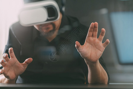 商人在现代办公室佩戴虚拟现实护目镜用智能手机使VR头盔的现代办公室使用智能手机背景图片