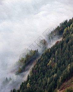 横跨阿尔卑斯山丘的有线汽车通龙多拉斯从迷雾云向顶端移动秋雾晨景图片流季节云和迷雾天气状况背景场背景图片