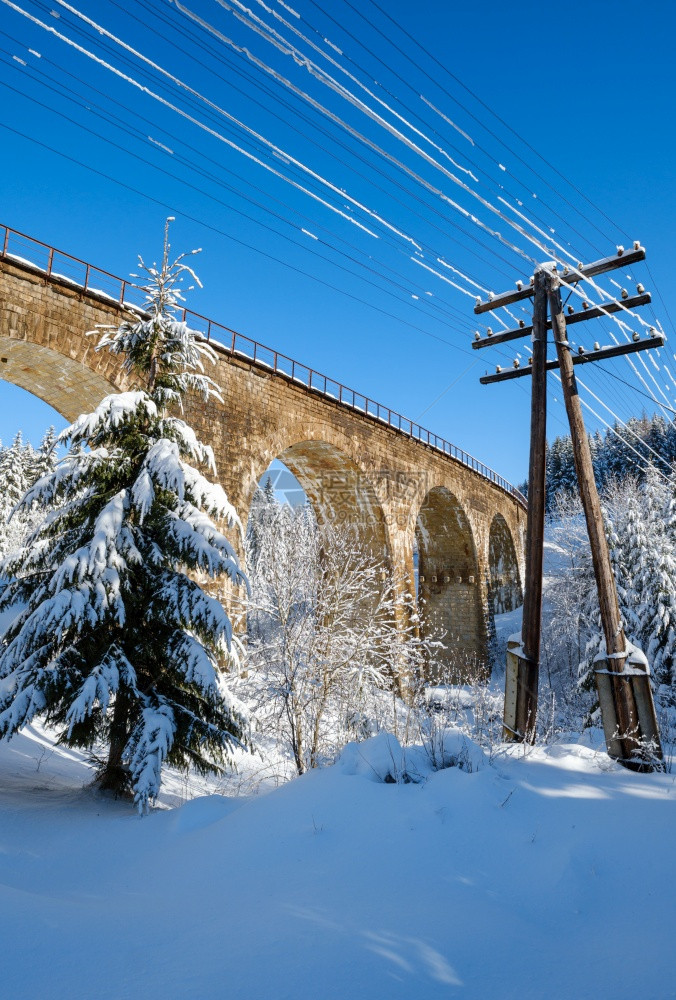 在山雪森林的铁路上建造石桥archbridge雪漂在路边树木和电线上漂浮图片