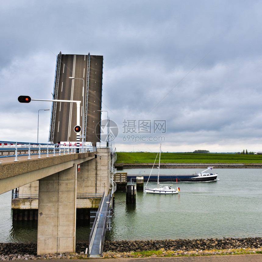 在荷兰运河上航行的大型驳船和游艇在荷兰运河对面的吊桥入口处有红灯图片