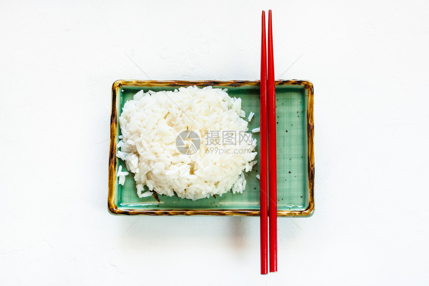 白色混凝土板上绿块的煮熟大米和红筷子的顶部视图有复制空间图片