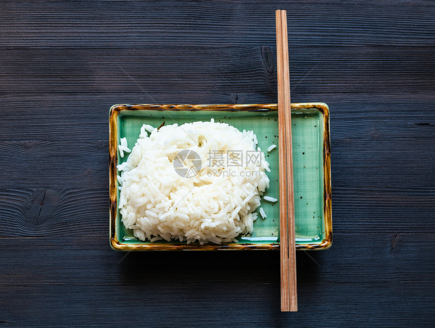 黑木板上绿色部分煮饭米和筷子的顶部视图图片