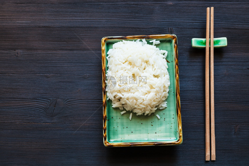 绿色板块上部分煮饭米和在黑色木桌复印空间上休息的筷子顶部视图图片