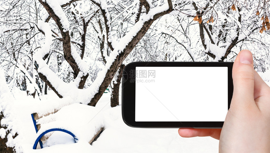 旅行概念莫斯科市冬季用智能手机在雪覆盖公共城市花园的雪覆盖公共城市花园中长椅的旅游照片带空白广告位置的剪贴板的智能手机图片