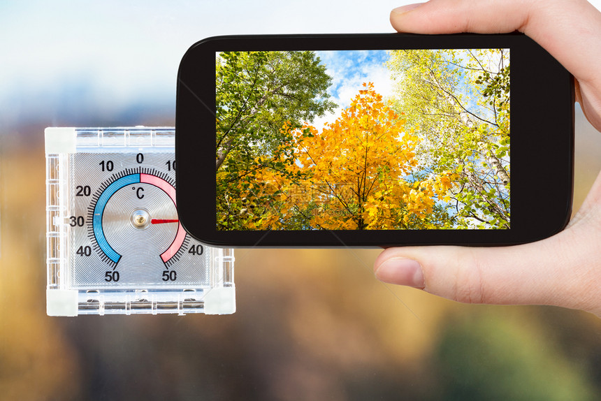 在俄罗斯莫科智能手机上热秋天家庭窗口拍摄黄树和户外温度计图片