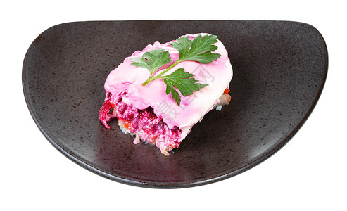 俄罗斯鲱鱼沙拉的一部分用欧芹叶装饰在黑色盘子上白色背景一份俄罗斯鲱鱼沙拉背景图片