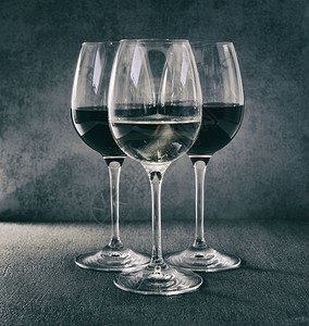 玻璃一杯白葡萄酒在两杯红葡萄酒前餐具图片