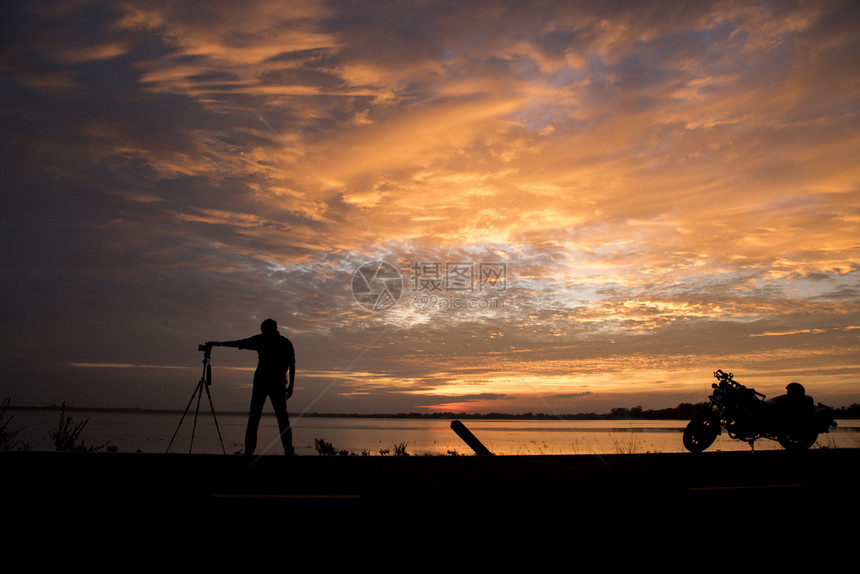 男人爱好席丽休埃特英俊摄影师在日落时拍一张带有专业相机的片一种图片