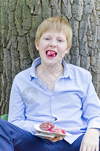 靠近男孩坐在树旁吃着甜点和胃口男白色的图片