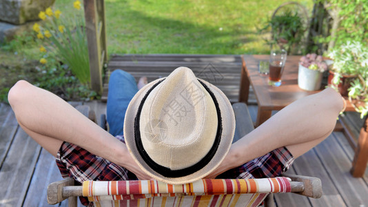年轻男子看见他背面戴着帽子在花园的阳台上放松假期坐着男人图片