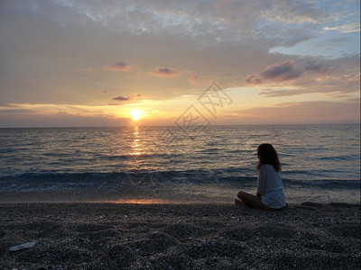 沉思日落时在希腊海滩冥想的年轻女子打坐的图片