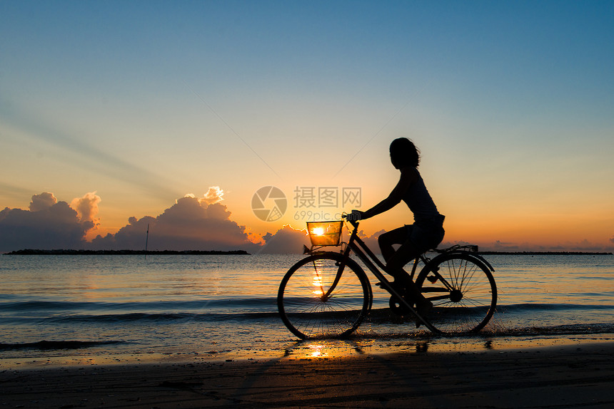 女孩在日出时海中骑自行车运动的海滩活力图片