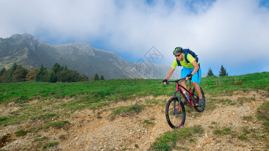 准备一种骑术名年轻男骑着山上自行车在草地下坡图片