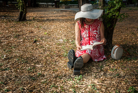 坐在草坪上倚着大树看书的女士图片