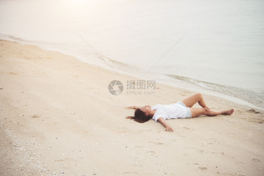 放松穿着白色T恤衫的年轻女子躺在海滩上微笑着享受自然女生活方式概念的自然快乐夏天美丽的图片