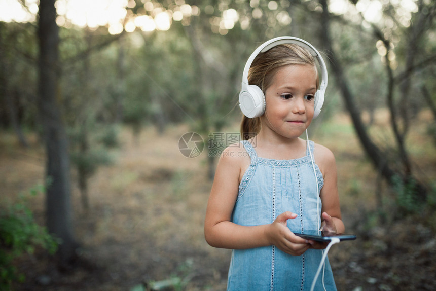 可爱的小朋友戴着耳机用手机听音乐图片