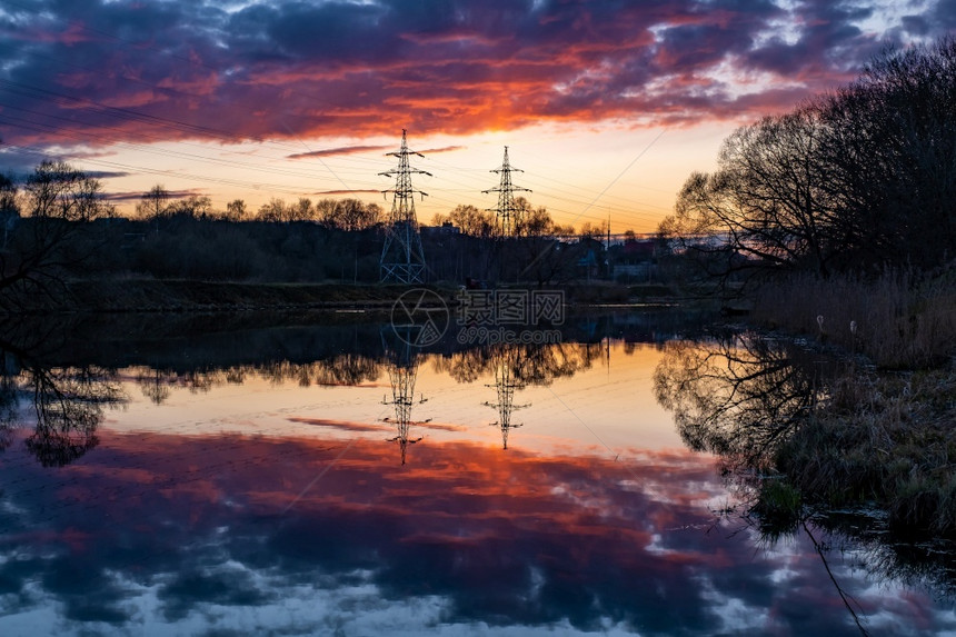 塔架一种轮廓两座电线塔对抗明亮的橙色日落和水中反射图片