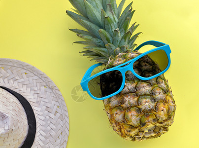 饮食蓝色的黄背景中带蓝太阳镜和草帽的菠萝有趣图片