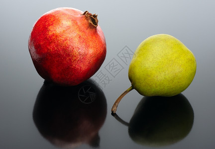 石榴和黑色背景的梨子有反射红色的水果酒图片