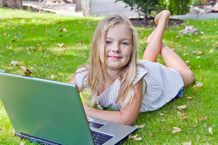 趴在草坪上看笔记本电脑的小女孩背景图片