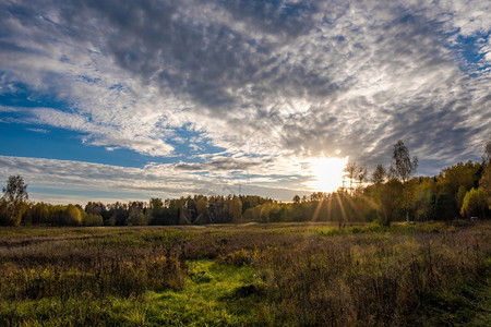 乌云下的阳光线落在秋天的田地上图片
