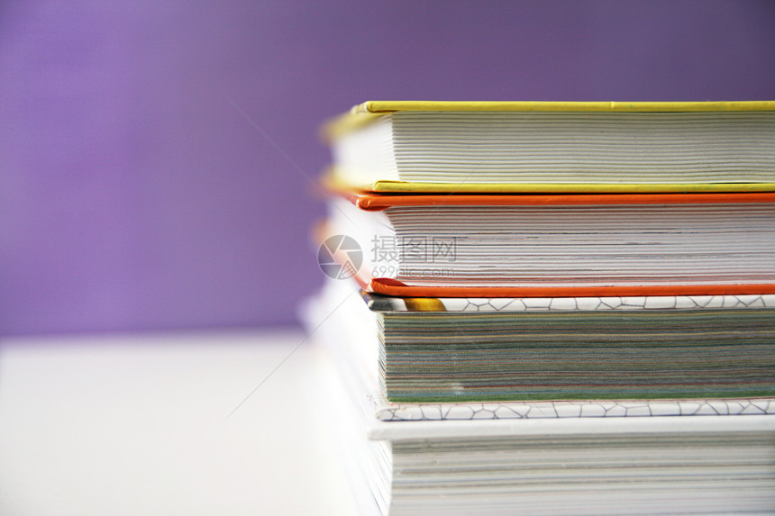 紫色的图书百科全在紫色背景复制空间的白桌子上藏着一堆儿科书本图片