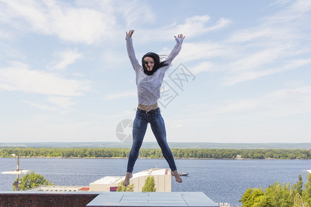 河水背景上年轻女跳跃的照片白色天空淑女图片