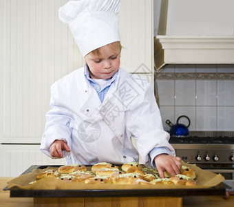 白色的托盘一个小男孩在厨房里烘烤和烧面包穿着一件粉和个厨师夹克袖子图片