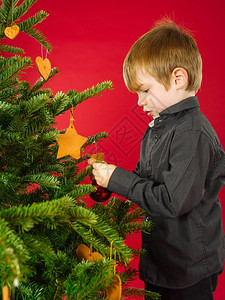 假期微笑快乐的一位男孩在圣诞树上挂着装饰物的照片图片
