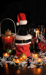 圣诞餐桌上一瓶红酒蜡烛球和眼镜之间桌子包雪背景图片