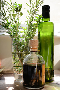 一瓶橄榄油和巴萨醋酸放在装满迷迭香和红菜的杯子旁边史密斯美食草药背景图片