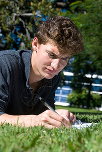 一名趴在大学校园草地上写字的男生图片