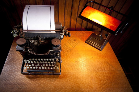 黄色的白生锈Wooden案桌被一盏黄灯旧照亮一辆历史生锈打字机和一张压实的白纸背景图片
