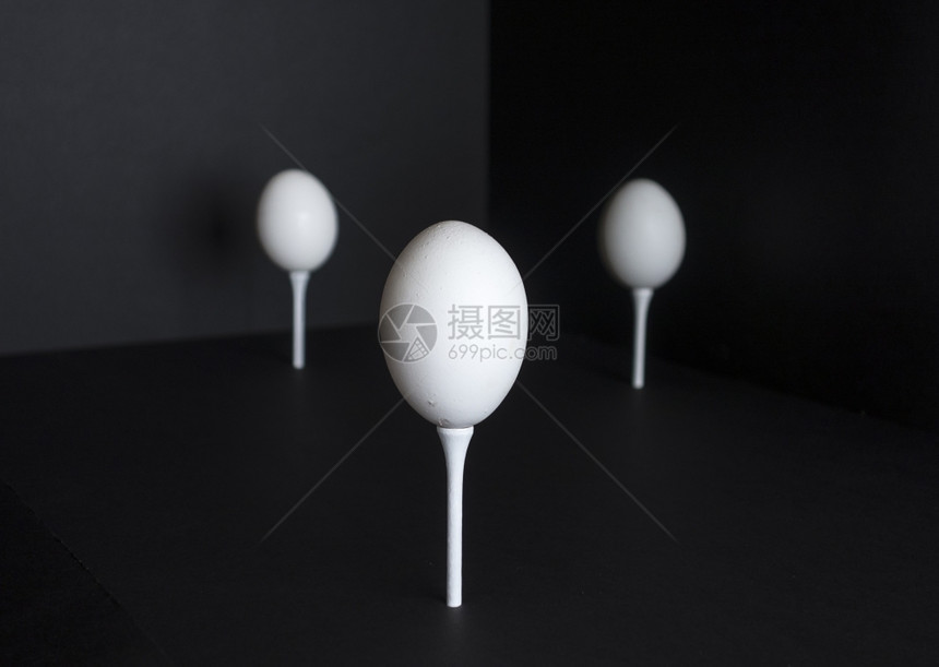 黑色的常设三个鸡蛋站在高尔夫球场黑色背景下突出显示人们图片