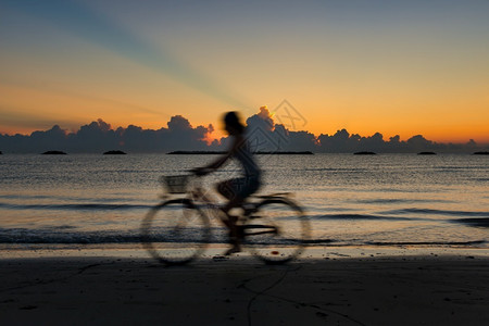 假期旅游黎明时在海滩骑自行车妇女产生模糊效果的轮椅放松图片