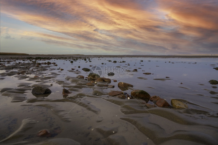 橙天空荷兰潮湿海滩上的石头和水以云彩为背景欧洲图片