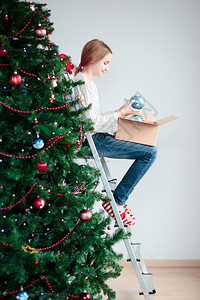 年轻女孩拿着一个球在家里装饰圣诞树年轻的喜悦松图片