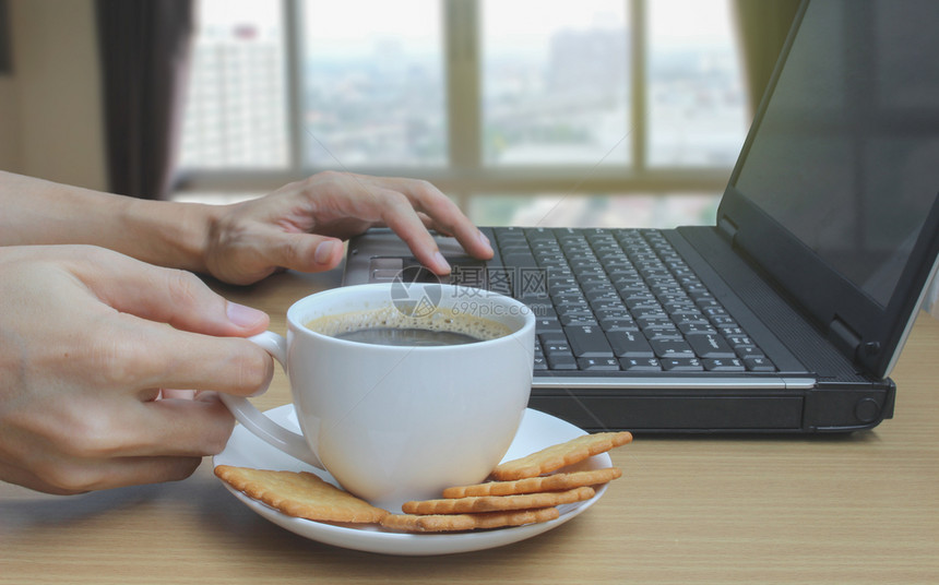 手喝咖啡使用笔记本电脑和模糊的卧室窗户背景饮料拿铁浓咖啡图片
