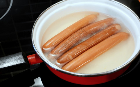 狗烹饪四根香肠红番茄在锅里热水中沸腾煮熟的图片