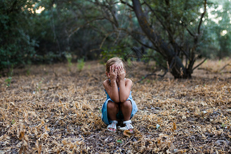 寂寞悲伤的小女孩蹲在森林里用手盖住她的脸用手盖住她的脸凉鞋覆盖天图片