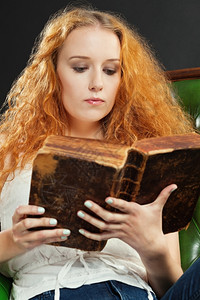 一位红卷发女在读旧书时头发坐着红色的图片