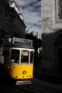 电车线阴影里斯本大约黄色电车在狭窄的街道上弯曲背景