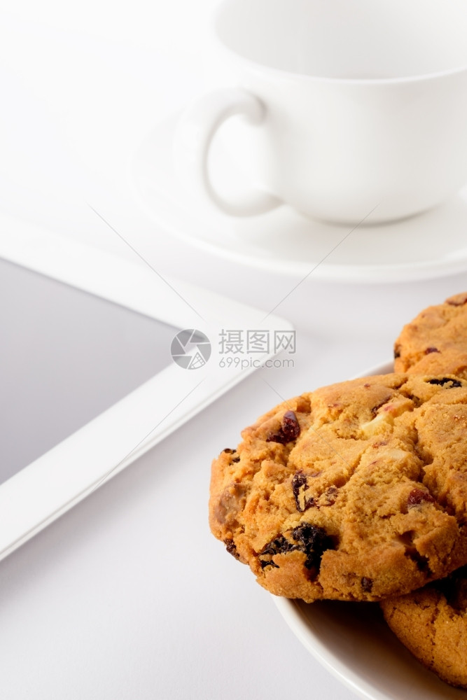 白色背景的自制饼干茶杯和平板食品电脑药片葡萄干图片