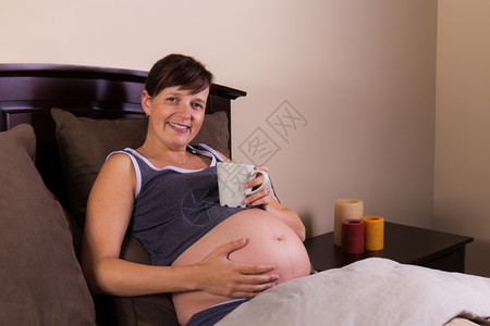 期待母亲在卧室喝咖啡享受她的肚子饮料婴儿图片