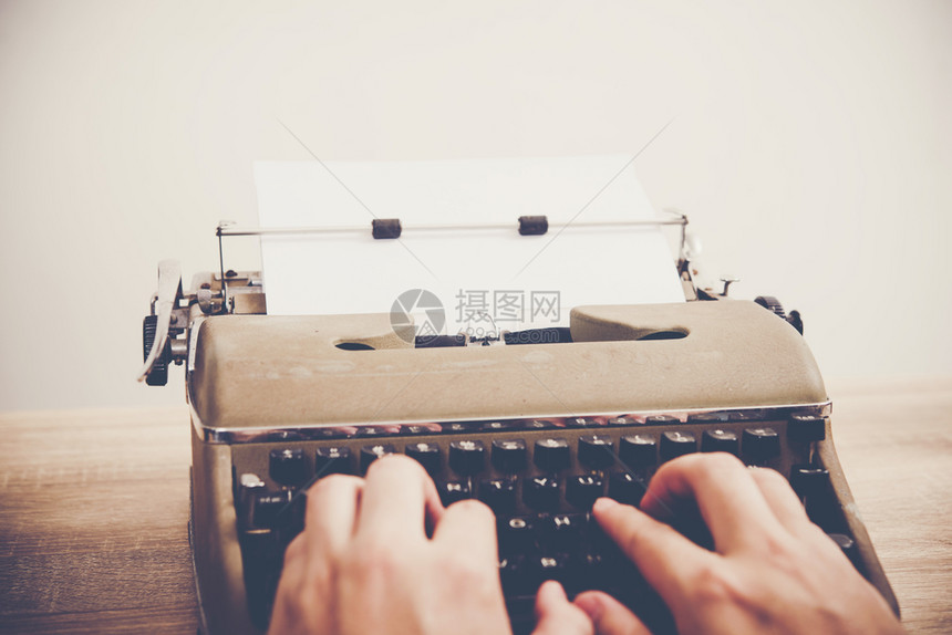 作者手打在木制桌上的老式打字机书工作图片