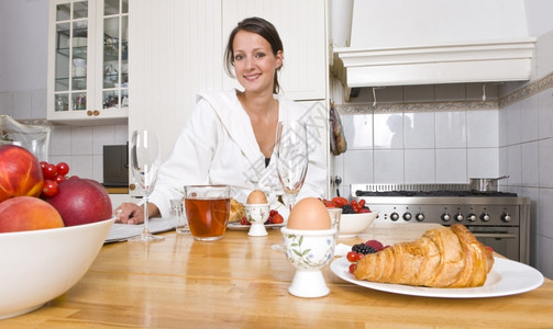棕色的年轻妇女在厨房柜台享受丰盛的早餐有水果羊角面包鸡蛋和早报纸女士背景