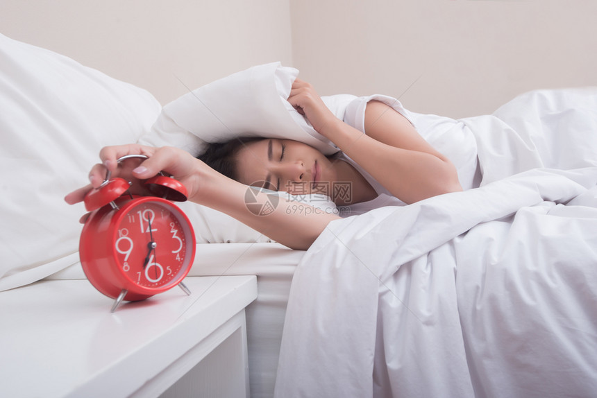 美丽的白色睡在床上年轻女人和卧室里的闹钟困图片