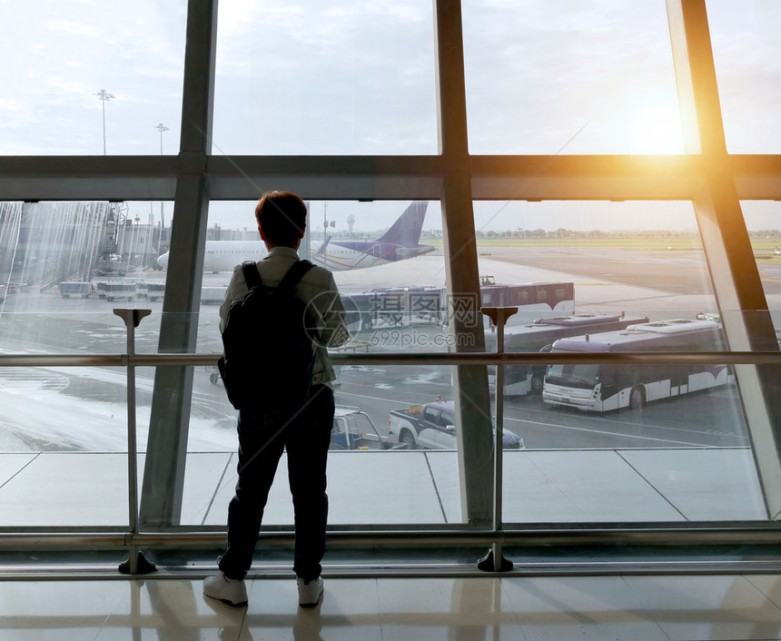 机场上带背包的年轻旅行者通过窗口看着等待飞行的机望着窗外看一眼户飞机场人们图片