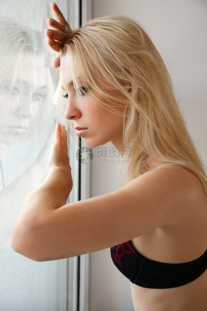 在窗户旁边的悲伤年轻女子肖像金发靠近女图片